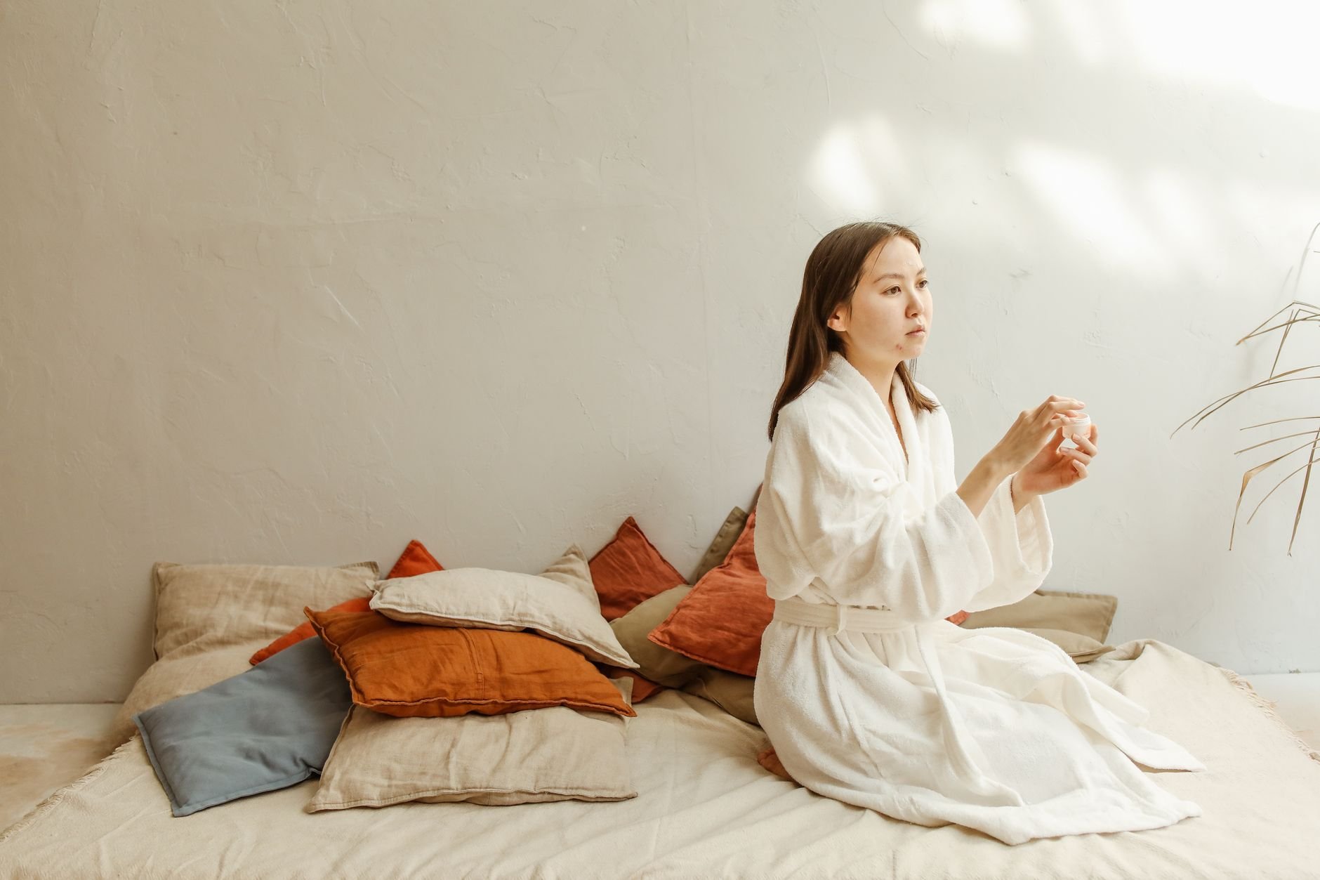 Asian woman practicing a calming skincare routine indoors with soft natural lighting.