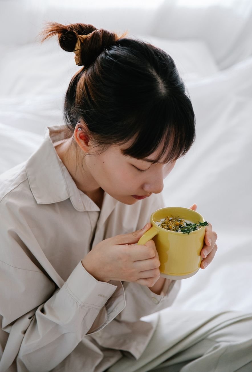 Asian woman savoring a warm herbal tea in a cozy indoor setting, conveying relaxation and tranquility.